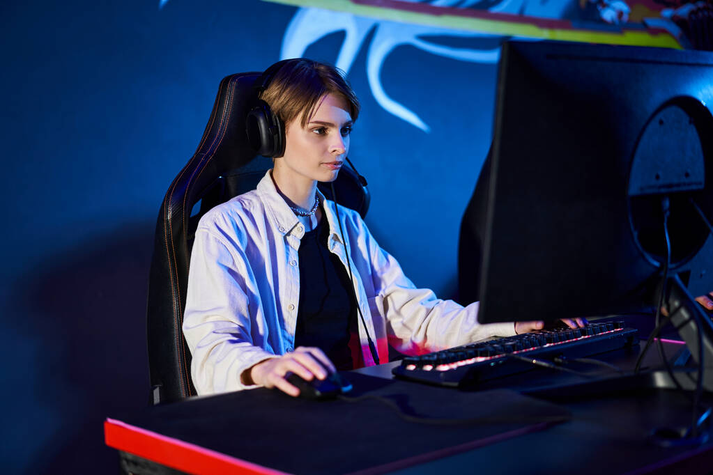 сфокусированный геймер с короткими волосами, смотрящий на компьютер в комнате с синим светом, киберспортсмен - Фото, изображение