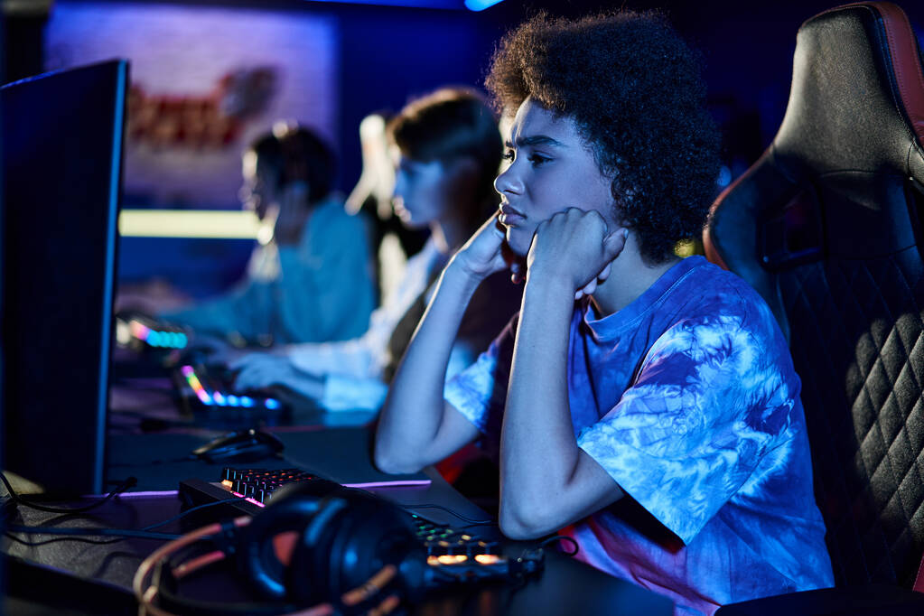 triest Afrikaans amerikaans vrouw kijken naar computer monitor en puffing wangen in blauw verlichte kamer - Foto, afbeelding