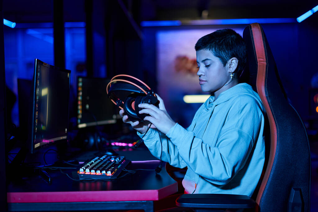 mladá žena uvedení sluchátka na stůl po hraní hry v modré osvětlené místnosti, kybersport - Fotografie, Obrázek