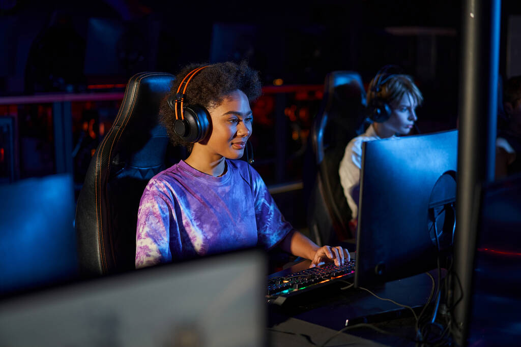 diverse female gamers in headphones looking at monitors while playing multiplayer computer game - Photo, Image