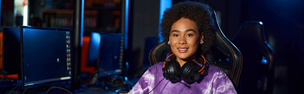 glückliche afrikanisch-amerikanische Spielerin mit Kopfhörern auf bequemem Gaming-Stuhl sitzend, Banner - Foto, Bild