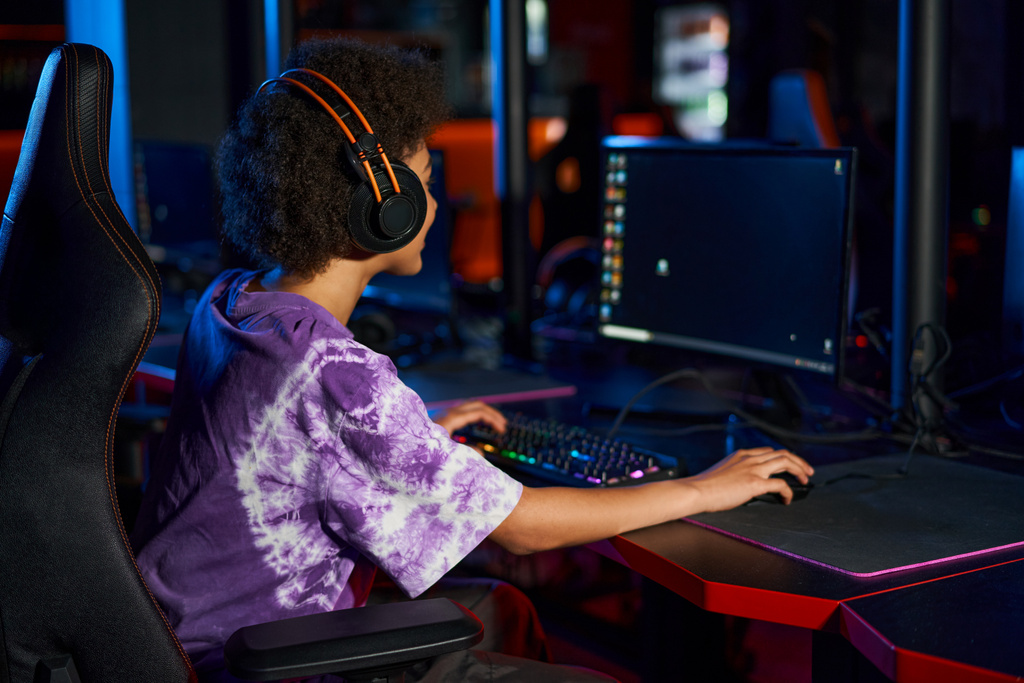 curly african american gamer in headphones playing computer game while looking at screen, cybersport - Photo, Image
