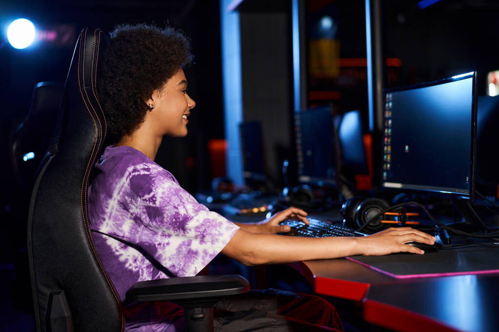 side view of happy african american woman sitting in gaming chair and looking at monitor, cybersport - Photo, Image
