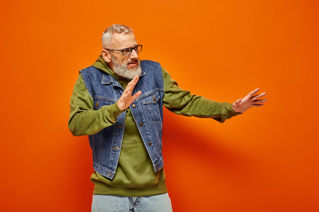 voorzichtig knap volwassen man met bril en baard in levendige hoodie poseren en kijken weg - Foto, afbeelding