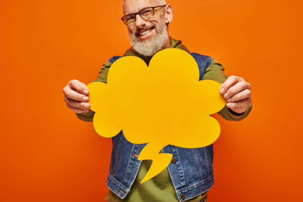 Сосредоточьтесь на желтом мыльном пузыре в руках веселого размытого зрелого человека, который смотрит в камеру - Фото, изображение