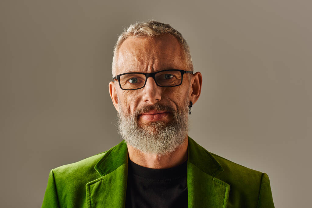 alegre atractivo hombre maduro en vibrante chaqueta verde con gafas y barba mirando a la cámara - Foto, Imagen