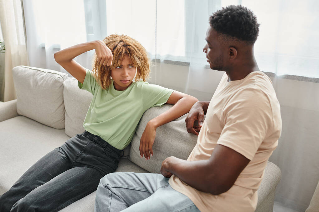 mulher afro-americana gesticulando enquanto olha para o namorado no sofá, comunicação não verbal - Foto, Imagem