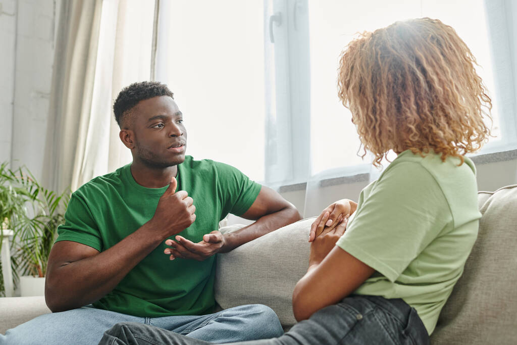 Afrikanisch-amerikanischer Mann zeigt Hilfsgeste, während er in der Nähe seiner Freundin mit Gebärdensprache kommuniziert - Foto, Bild