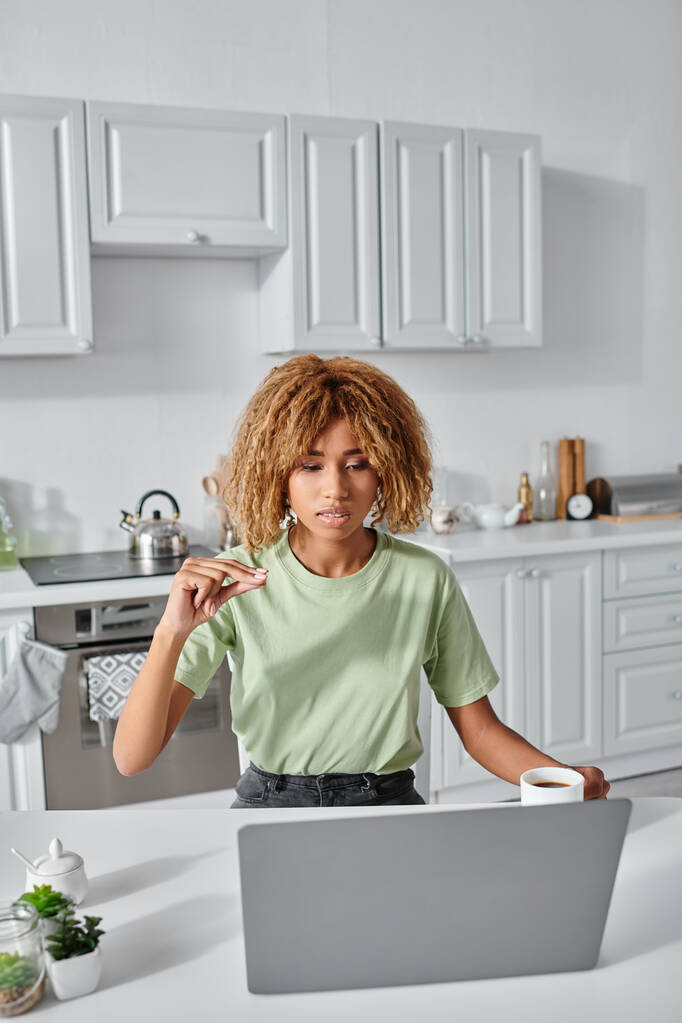 focada mulher afro-americana usando linguagem de sinais durante videochamada e segurando xícara de café - Foto, Imagem