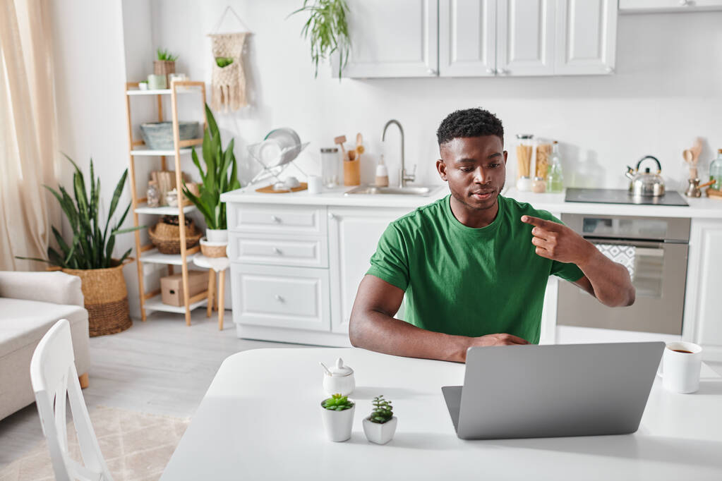 kuuro afrikkalainen amerikkalainen mies vihreässä t-paidassa käyttäen viittomakieltä online-viestintään kannettavalla tietokoneella - Valokuva, kuva