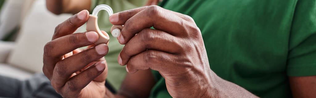 bannière recadrée de prothèse auditive dans les mains sur l'homme noir, afro-américain tenant un dispositif médical - Photo, image