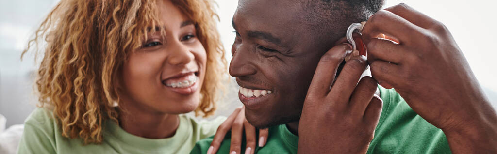 dove en gelukkige Afrikaan amerikaanse man met gehoorapparaat in de buurt van vriendin, gezondheid apparaat banner - Foto, afbeelding