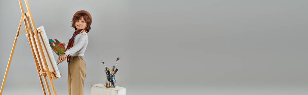 χαρούμενο αγόρι διερευνά δημιουργικό δυναμικό του, καλλιτέχνης σε μπερέ με ζωγραφική παλέτα κοντά easel, banner - Φωτογραφία, εικόνα