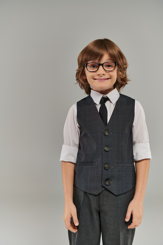 κομψό αγόρι στέκεται με αυτοπεποίθηση, πουκάμισο κουμπωμένο στο γιακά και γιλέκο προσθέτοντας μια πινελιά στο βλέμμα του - Φωτογραφία, εικόνα