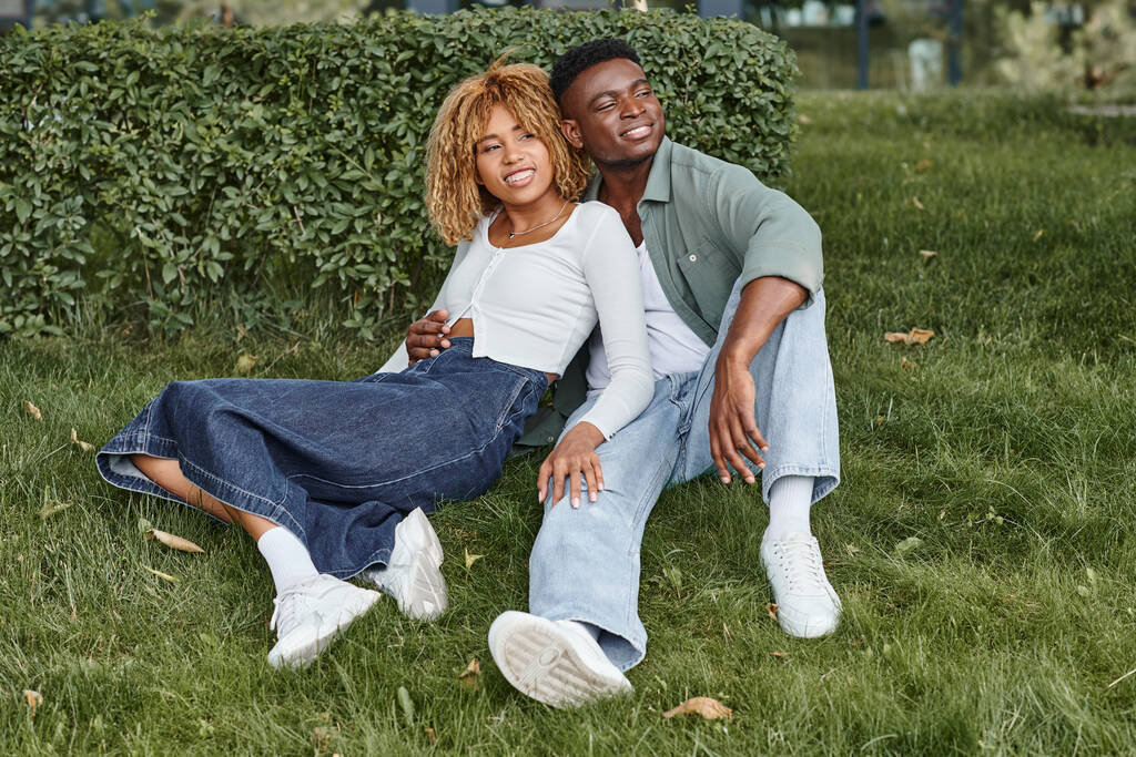 Χαρούμενο ζευγάρι Αφροαμερικανών που αγκαλιάζονται και κάθονται μαζί στο πράσινο γρασίδι, ευτυχία - Φωτογραφία, εικόνα
