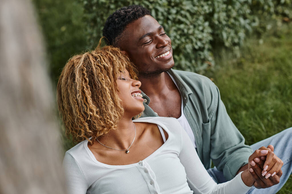 animado afro-americano mulher em aparelho de mãos dadas com namorado enquanto sentado no parque - Foto, Imagem