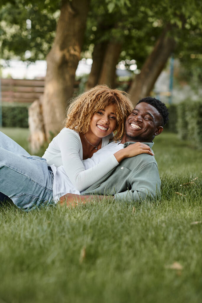 fröhliches afrikanisch-amerikanisches Paar, das Zeit miteinander verbringt, während es im Gras liegt - Foto, Bild