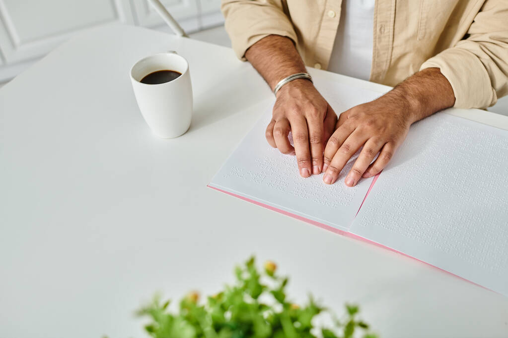 abgeschnittene Ansicht eines indischen Blinden in bequemer Kleidung, der am Tisch sitzt und Blindenschrift liest, behindert - Foto, Bild