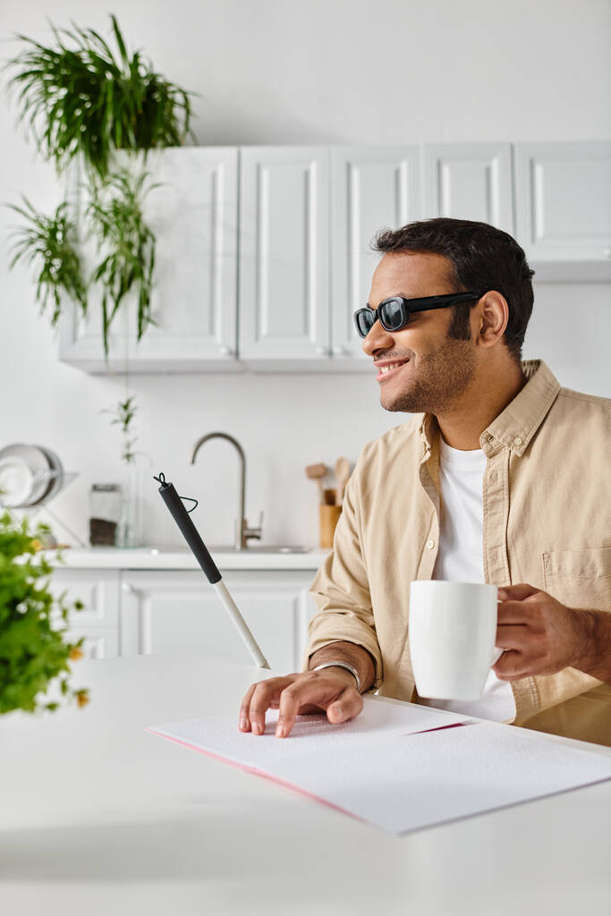 fröhlicher blinder indischer Mann in lässiger Kleidung mit Kaffee und Gehstock beim Lesen des Braillecodes - Foto, Bild