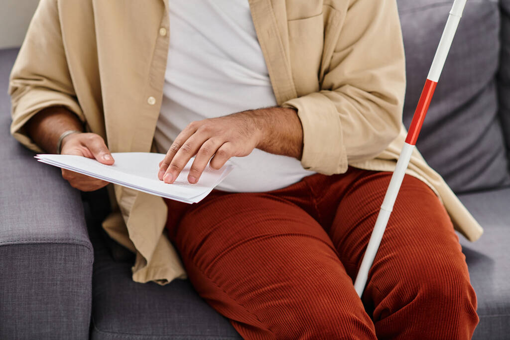 Ausgeschnittene Ansicht eines blinden indischen Mannes in Freizeitkleidung, der auf dem Sofa sitzt und Brailleschrift-Code liest - Foto, Bild
