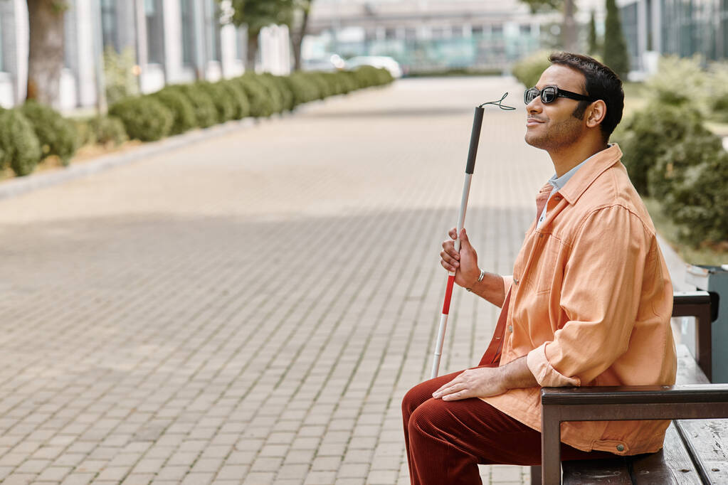 homem cego indiano feliz em jaqueta laranja sentado fora no banco com bengala e óculos - Foto, Imagem