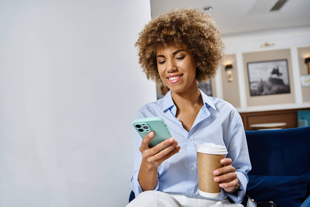 glücklich lockige Afroamerikanerin mit Coffee to go und Smartphone in Hotellobby - Foto, Bild