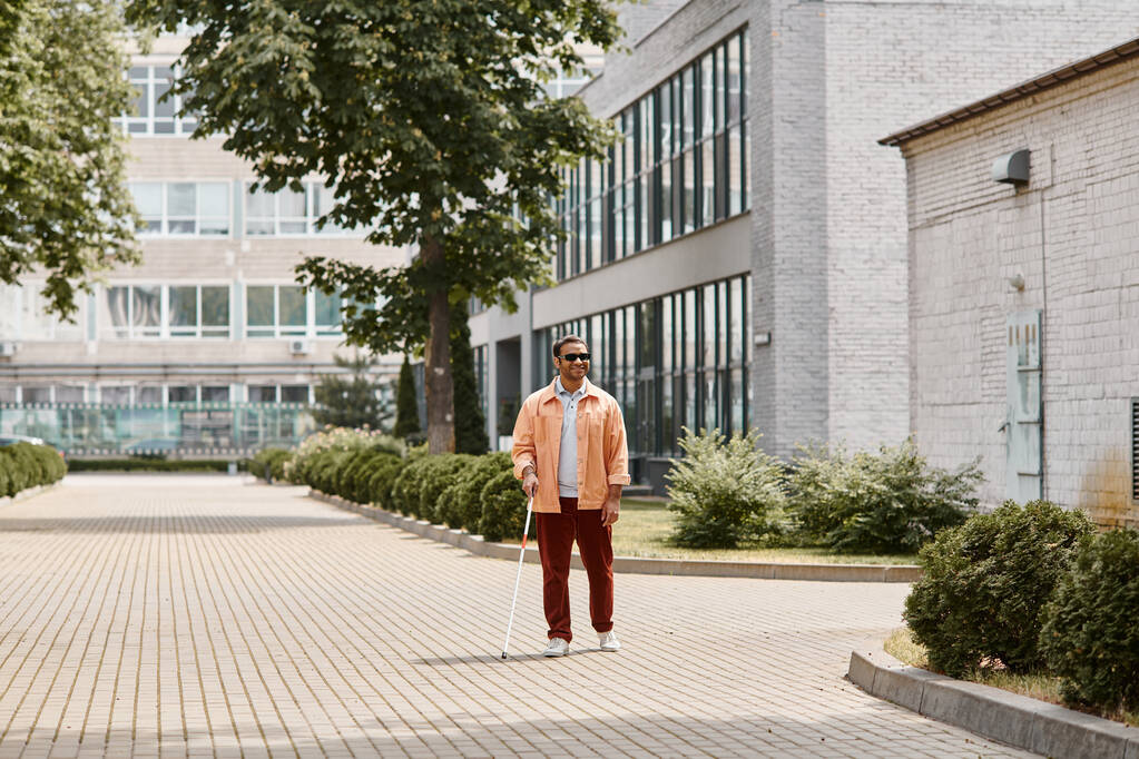 vidám indiai vak férfi narancssárga dzsekiben szemüveggel és sétapálcával sétál a parkban - Fotó, kép