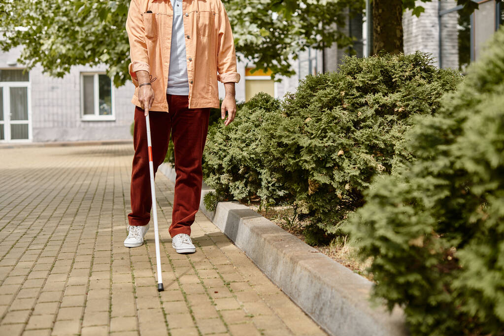 cropped view of indian disabled man in orange jacket with walking stick taking walk in park - Photo, Image