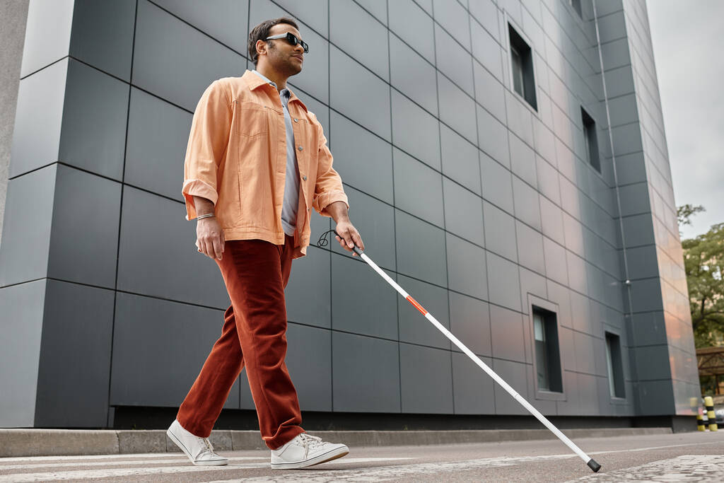 heureux aveugle indien en veste orange avec bâton de marche et des lunettes avec mur gris sur fond - Photo, image