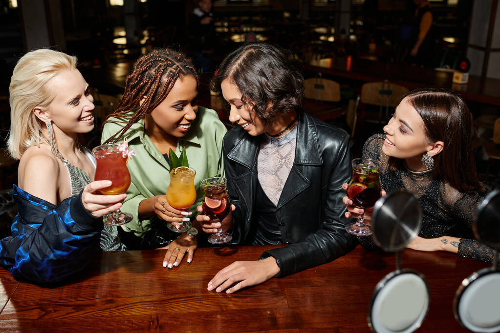 vrolijke en modieuze multiraciale vrouwen toasten met cocktails in de moderne nachtbar, vrije tijd - Foto, afbeelding