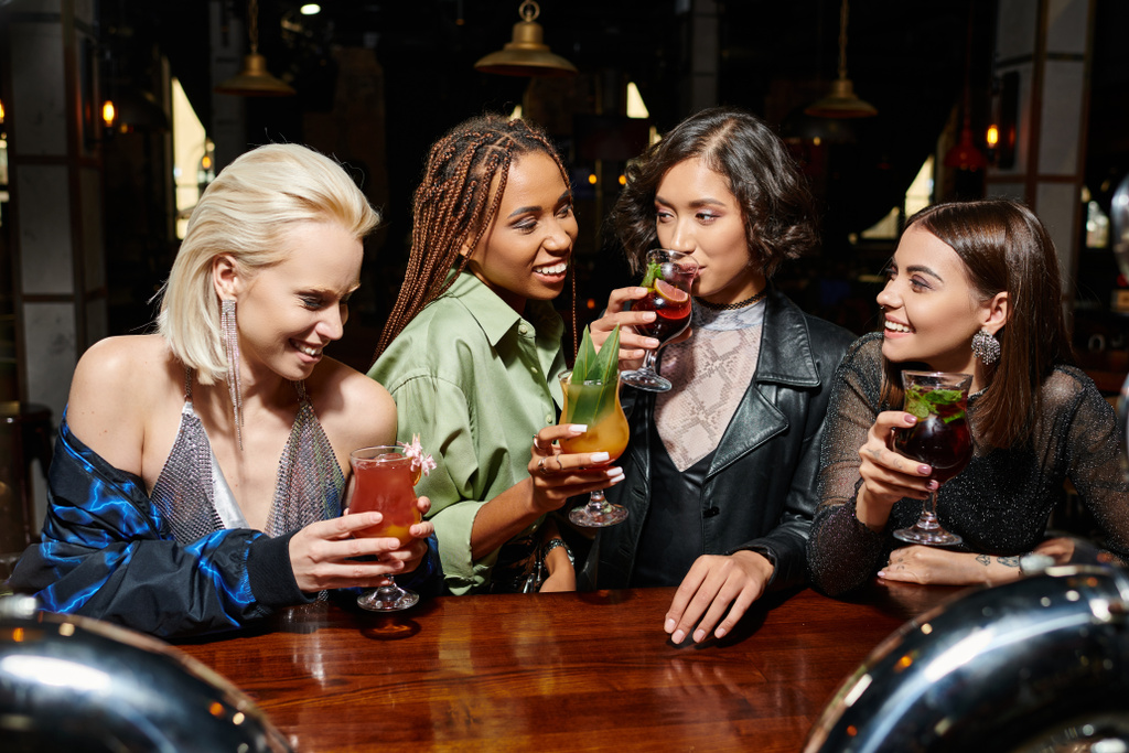 junge asiatische Frau trinkt Cocktail in der Nähe fröhlicher multiethnischer Freundinnen in Bar, Party-Zeit - Foto, Bild