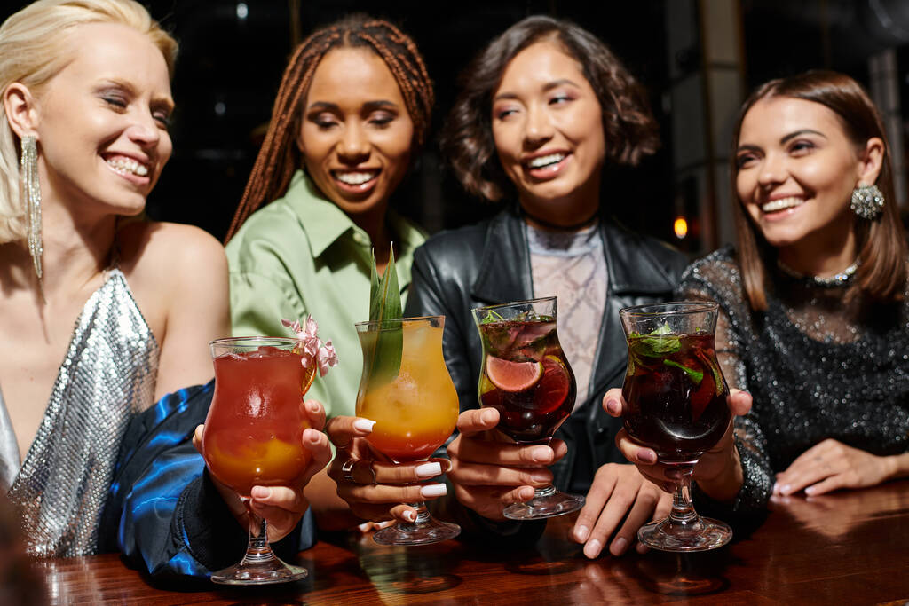 χαρούμενες και γοητευτικές πολυπολιτισμικές φίλες που κρατούν νόστιμα κοκτέιλ στο μπαρ, λαμπερό πάρτι - Φωτογραφία, εικόνα