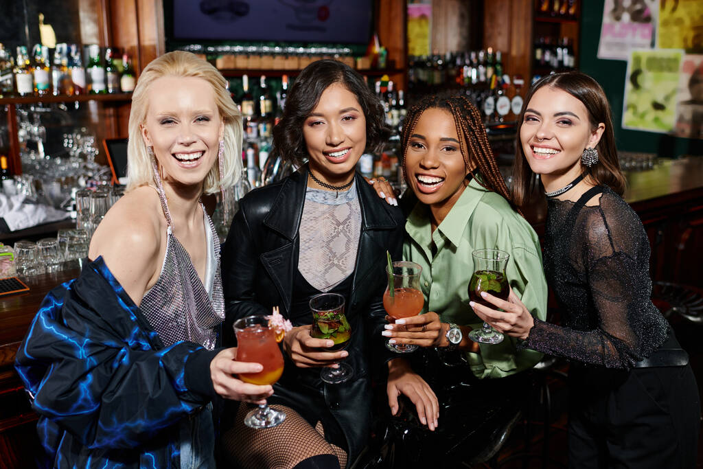 namoradas multiétnicas alegres e elegantes com óculos de cocktail olhando para a câmera no bar - Foto, Imagem