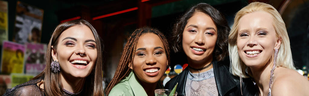 jovens sedutoras namoradas multirraciais sorrindo para a câmera durante a festa no bar moderno, banner - Foto, Imagem