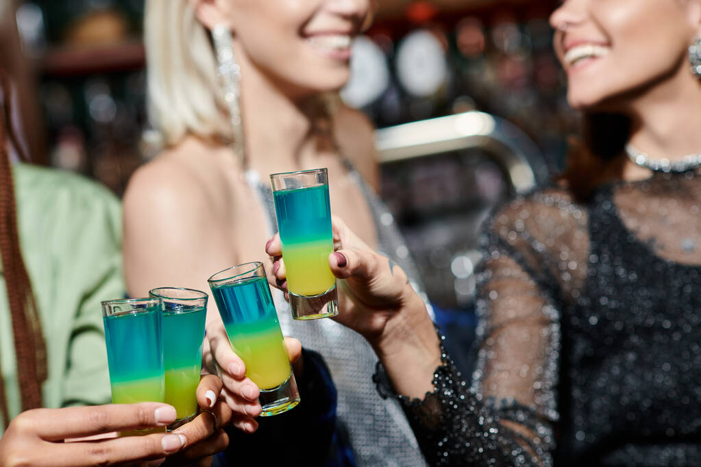 cropped view of blurred multiracial female friends clinking shot glasses in modern bar, party - Photo, Image