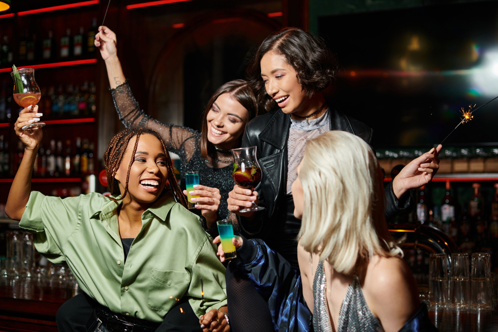 gelukkige multiculturele vriendinnen met glanzende sterretjes en cocktailglazen in bar, feestelijke sfeer - Foto, afbeelding