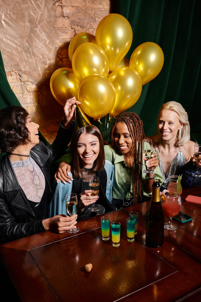 felice donne multietniche eleganti con champagne vicino palloncini d'oro e cocktail nel bar, compleanno - Foto, immagini