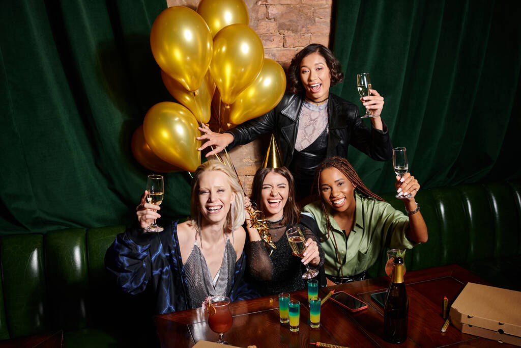 веселі мультикультурні подружки з шампанським дивляться на камеру і святкують день народження в барі - Фото, зображення