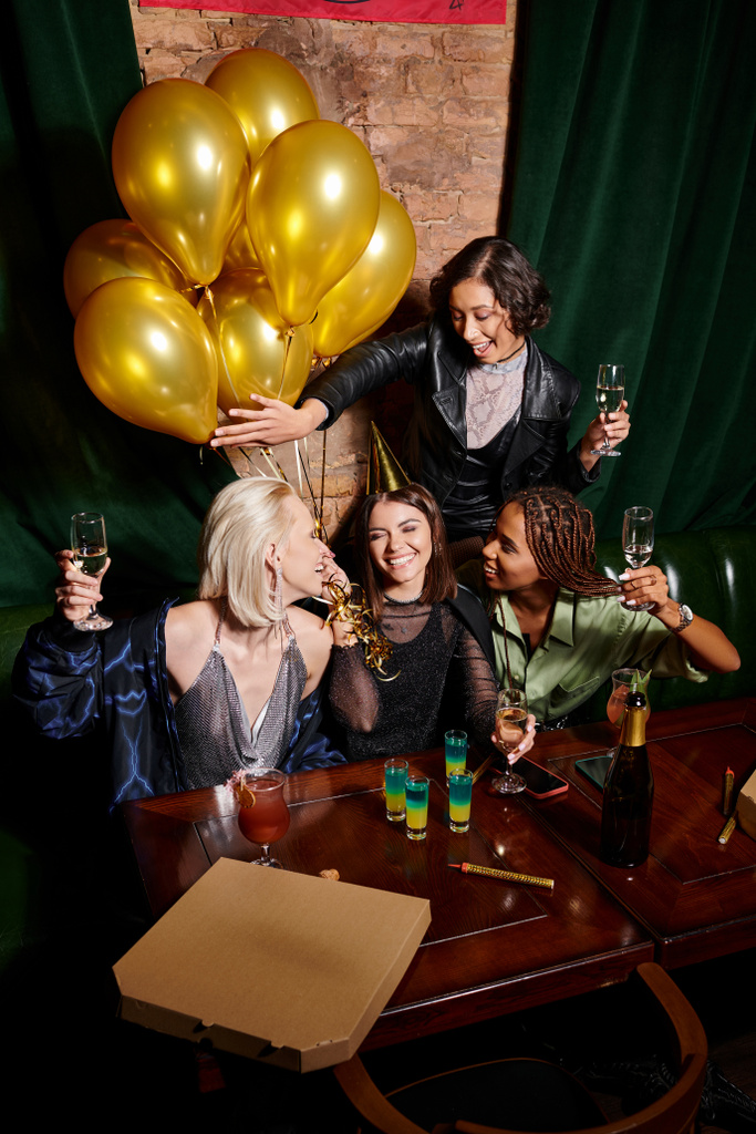 glamorous multiethnic women celebrating birthday with alcohol drinks and golden balloons in bar - Photo, Image