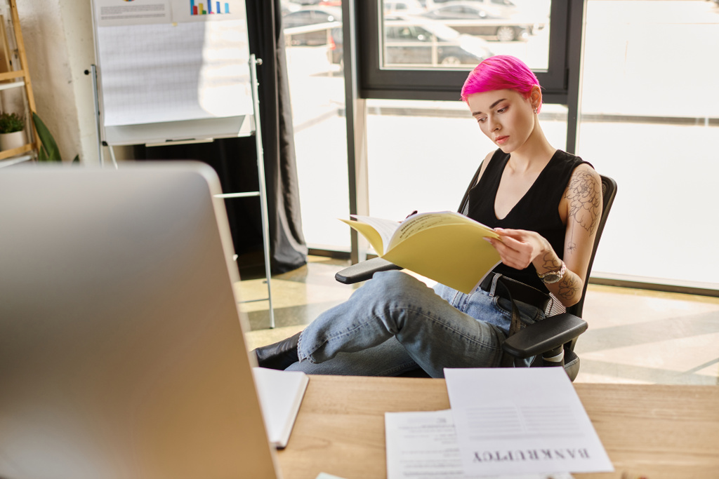 junge Arbeiterin in lässigem Outfit arbeitet hart mit Dokument mit dem Wort Konkurs auf dem Schreibtisch - Foto, Bild