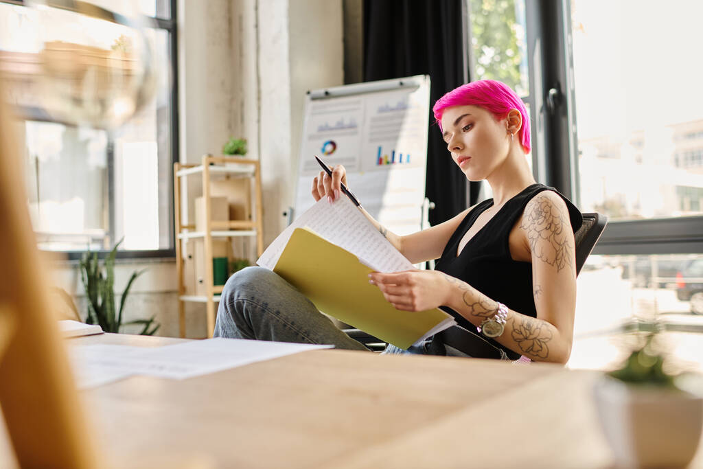 figyelmes fiatal nő rózsaszín hajjal és tetoválásokkal ül és nézi a jegyzeteit, üzleti koncepció - Fotó, kép