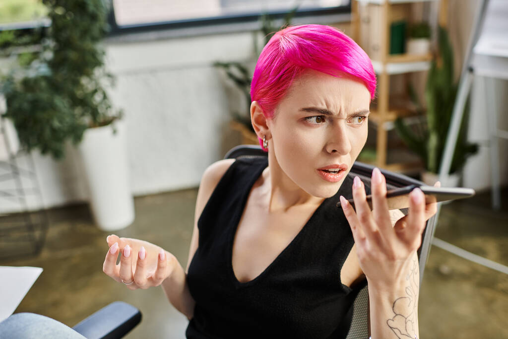 Ενοχλημένη όμορφη επιχειρηματίας με τατουάζ και ροζ μαλλιά που μιλάει δυστυχισμένα από το τηλέφωνο στο γραφείο - Φωτογραφία, εικόνα