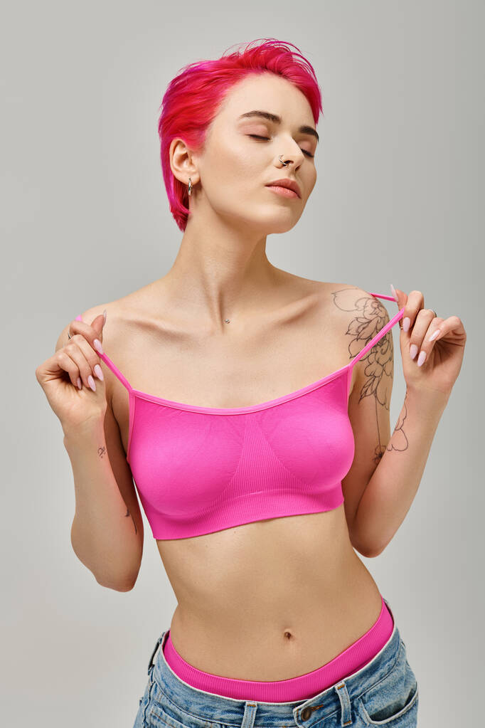 jonge vrouw in roze gewas top en jeans met tatoeages poseren met gesloten ogen, mode concept - Foto, afbeelding