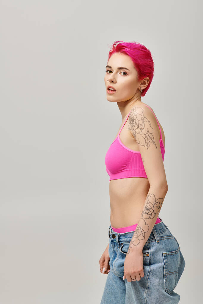 svůdná krátkovlasá žena s tetováním pózující na šedém pozadí a dívající se na kameru, móda - Fotografie, Obrázek