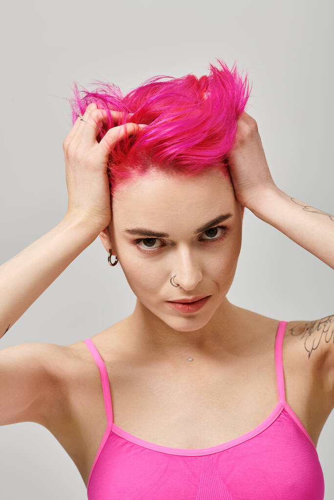Porträt einer verführerischen jungen Frau mit rosa Haaren und Tätowierungen, die posiert und ihre Haare berührt, Mode - Foto, Bild