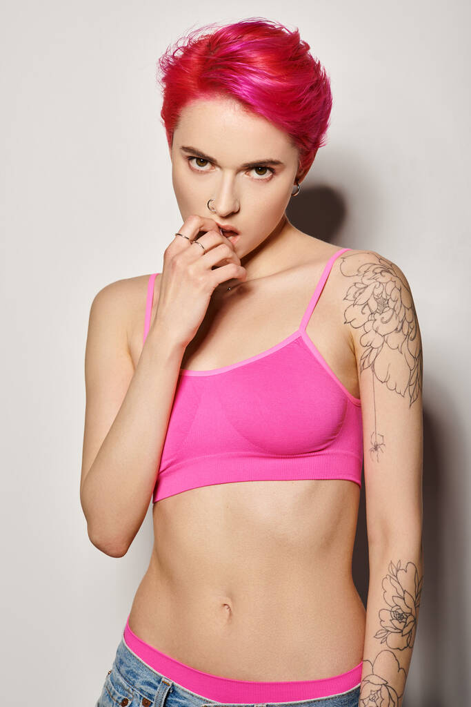 tatuoitu ja lävistetty nainen vaaleanpunaiset hiukset ja poseeraa kirkas sato alkuun ja farkut harmaalla pohjalla - Valokuva, kuva