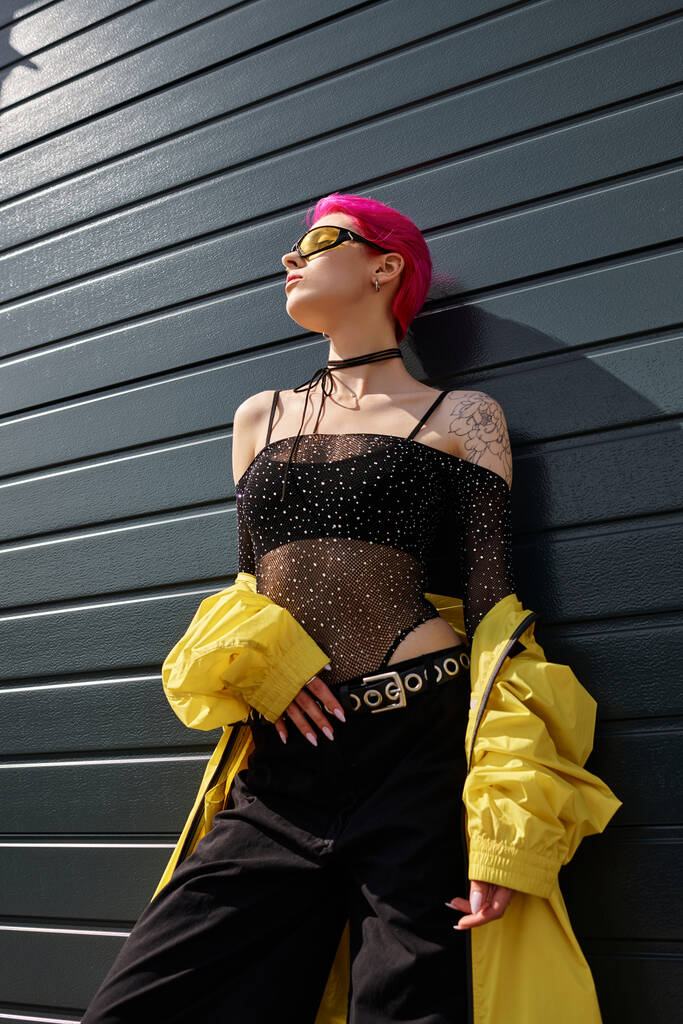 jovem de cabelos rosa em óculos de sol amarelos e roupa elegante posando ao ar livre, visão de baixo ângulo - Foto, Imagem