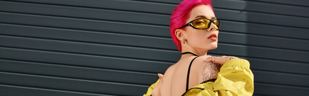 rózsaszín hajú fiatal nő sárga napszemüveg és divatos ruhát pózol, és nézi a kamera, banner - Fotó, kép