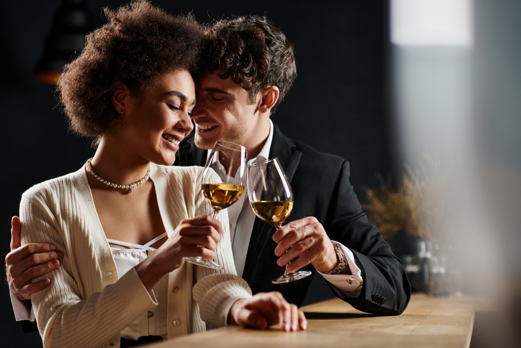szczęśliwy międzyrasowy para brzęczenie szklanki białego wina podczas randki w święto Walentynki, romans - Zdjęcie, obraz