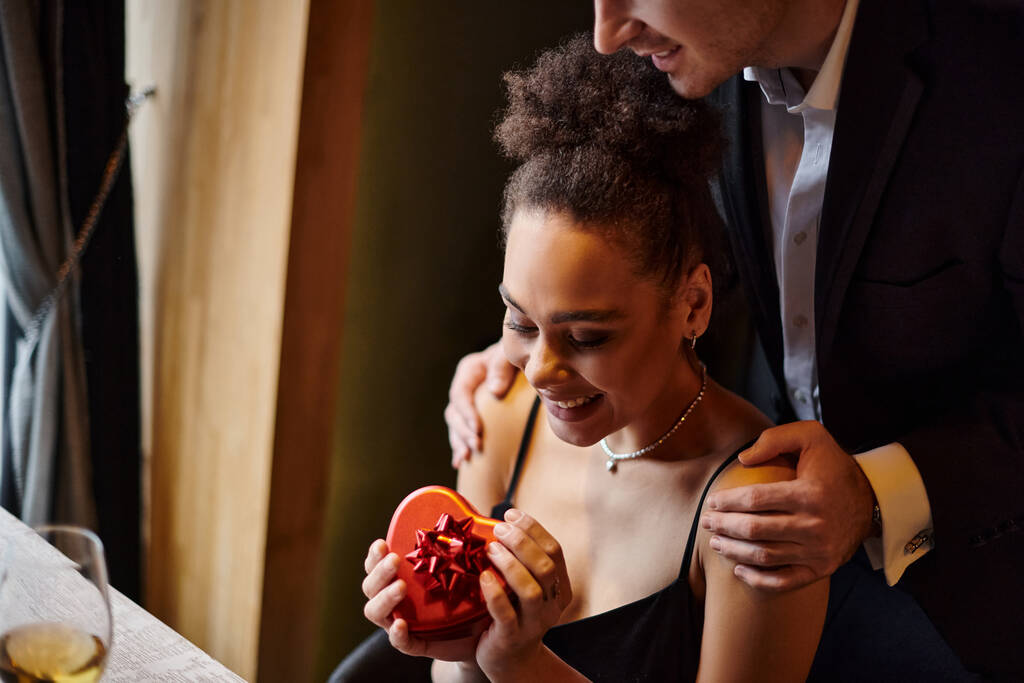 muž objímání šťastný africký americký přítelkyně po darování červené srdce ve tvaru krabice na Valentýna - Fotografie, Obrázek